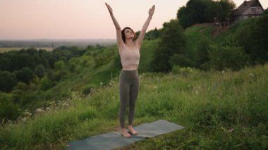 Ağır çekim: Eşofmanlı genç kadın dağlarda yoga pozisyonu alıyor. Kamera bir şeyler yaratıyor. Dışarıda yoga yapan bir kadın. Yoga yapan bir kadın..