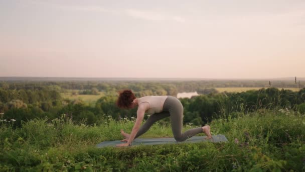 Zwolniony ruch: młoda kobieta w dresie ćwiczy jogę w górach. Kamera się porusza. Kobieta ćwicząca jogę na świeżym powietrzu. Kobieta robi ćwiczenia jogi. — Wideo stockowe