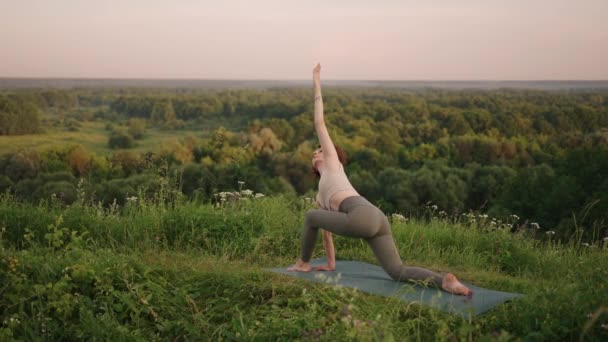 Lassú mozgás: fiatal nő melegítőben jóga pozíciót gyakorol a hegyekben. A kamera alkotás közben mozog. Egy nő, aki kint jógázik. Jóga gyakorlatokat végző nő. — Stock videók