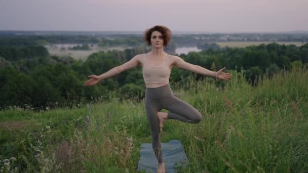 Movimiento lento: Mujer joven en chándal practica la posición de yoga en las montañas. La cámara se mueve creando. Mujer practicando yoga al aire libre. Mujer haciendo ejercicios de yoga. — Vídeos de Stock