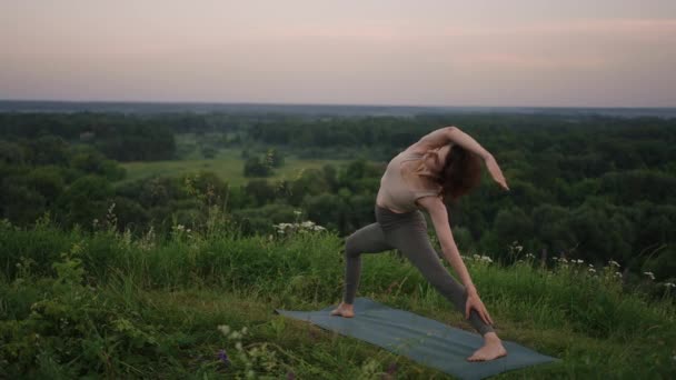 Movimiento lento: Mujer joven en chándal practica la posición de yoga en las montañas. La cámara se mueve creando. Mujer practicando yoga al aire libre. Mujer haciendo ejercicios de yoga. — Vídeos de Stock