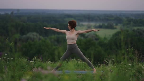 Movimiento lento: Mujer joven en chándal practica la posición de yoga en las montañas. La cámara se mueve creando. Mujer practicando yoga al aire libre. Mujer haciendo ejercicios de yoga. — Vídeo de stock