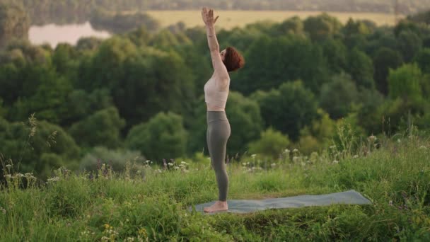 Lassú mozgás: fiatal nő melegítőben jóga pozíciót gyakorol a hegyekben. A kamera alkotás közben mozog. Egy nő, aki kint jógázik. Jóga gyakorlatokat végző nő. — Stock videók