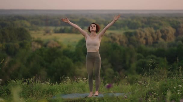 Ağır çekim: Eşofmanlı genç kadın dağlarda yoga pozisyonu alıyor. Kamera bir şeyler yaratıyor. Dışarıda yoga yapan bir kadın. Yoga yapan bir kadın.. — Stok video