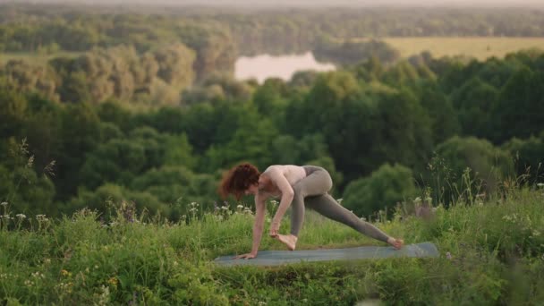 Ağır çekim: Eşofmanlı genç kadın dağlarda yoga pozisyonu alıyor. Kamera bir şeyler yaratıyor. Dışarıda yoga yapan bir kadın. Yoga yapan bir kadın.. — Stok video