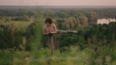 Ağır çekimde, genç bir kadın yoga egzersizlerini dengeleme ve üstte germe yaparak gerçekleştiriyor. Beden ve ruhun sakin ve huzurlu dengesi. Vücut eğilir ve eğilir.