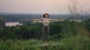 Genç bir kadın sabahın köründe yogayı önceden hazırlıyor. Kadın dağ zirvesinde yoga hareketleri yapıyor. Dağlık alanda dinginlik ve yoga, meditasyon.