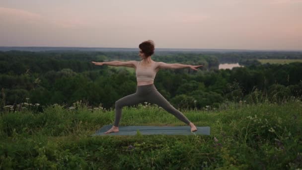 Dalam gerakan lambat, seorang wanita muda melakukan latihan yoga dengan melakukan penyeimbangan dan peregangan di atas. Tenang dan damai keseimbangan tubuh dan jiwa. Tubuh membungkuk dan membungkuk — Stok Video