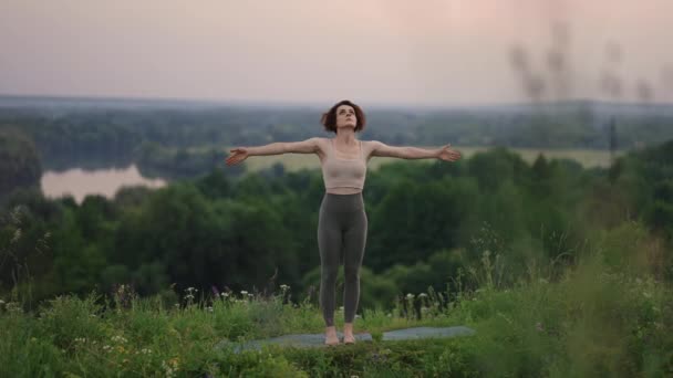 Ung kvinna förebereder yoga i fjällen i gryningen. Kvinna utför yogarörelser på bergstoppen. Lugn och yoga tränar på bergskedja, meditation — Stockvideo