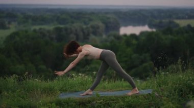 Ağır çekimde, genç bir kadın yoga egzersizlerini dengeleme ve üstte germe yaparak gerçekleştiriyor. Beden ve ruhun sakin ve huzurlu dengesi. Vücut eğilir ve eğilir.