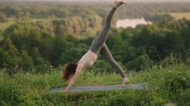 Ağır çekimde, genç bir kadın yoga egzersizlerini dengeleme ve üstte germe yaparak gerçekleştiriyor. Beden ve ruhun sakin ve huzurlu dengesi. Vücut eğilir ve eğilir.