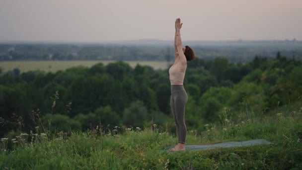 Ağır çekimde, genç bir kadın yoga egzersizlerini dengeleme ve üstte germe yaparak gerçekleştiriyor. Beden ve ruhun sakin ve huzurlu dengesi. Vücut eğilir ve eğilir. — Stok video