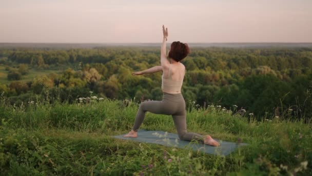 I slow motion utför en ung kvinna yogaövningar genom att balansera och stretcha ovanpå. Lugn och lugn balans mellan kropp och själ. Kroppsböjar och böjar — Stockvideo