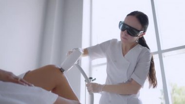 Güzellik salonunda lazer epilasyonu ve kozmetoloji. Kozmetoloji, spa ve saç temizleme konsepti. Kadın bacaklarının lazer tüy çıkarma prosedürü. Eldivenli doktor.