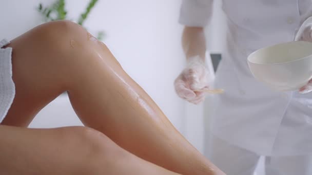 Use uma vara para aplicar um gel hidratante nas pernas dos clientes antes da depilação a laser nas pernas. O médico prepara as pernas para a depilação a laser em um salão de beleza — Vídeo de Stock