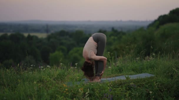 En ung kvinne som øver på yoga i naturen. Ung kvinnes posisjon å meditere utendørs – stockvideo
