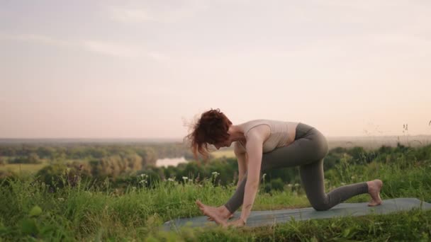 Genç bir kadın, ormanın tepesinde bir nehrin arka planına ve orman manzarasına karşı yoga egzersizleri yapıyor. Beden ve ruh dengesi, rahatlama ve meditasyon — Stok video