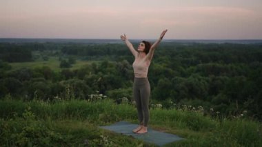 Genç bir kadın, ormanın tepesinde bir nehrin arka planına ve orman manzarasına karşı yoga egzersizleri yapıyor. Beden ve ruh dengesi, rahatlama ve meditasyon 