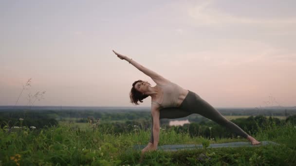 Nuori nainen harjoittelee joogaa luonnossa. Nuori nainen asema nauttii meditointi ulkona — kuvapankkivideo