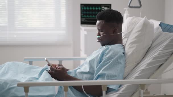 Afrikai férfi páciens okos telefonnal fekszik az ágyon. Afrikai beteg telefonon beszél a kórházi szobában — Stock videók