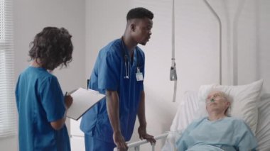 Yatakta yatan kıdemli hasta hastane odasında iki Afrikalı Amerikalı doktorla konuşuyor. Sağlık ve sigorta konsepti. Doktor yaşlı hastayı hastane yatağında rahatlatıyor ya da sağlık danışmanlığı yapıyor..