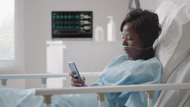 Black woman Patient in Hospital with Saline Solution Volumetric Infusion Pump using mobile phone on examination couch. African women lying in hospital bed with smart mobile phone while in hospital. — Stock Video