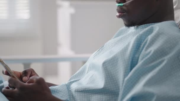 Afrikalı erkek hasta yatakta yatarken akıllı telefon kullanıyor. Afrikalı hasta hastane odasında telefon görüşmesi yapıyor. — Stok video