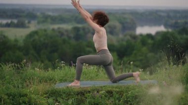 Bir yoga ustası denge ve esneme egzersizleri yapar. Ormandaki dağlarda yoga yapan bir kızın huzur ve rahatlığı.