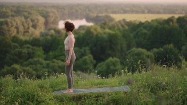 Kadın gün doğumunda çam ormanında yoga yapıyor. Genç ruhani kızın silueti Lotus 'ta meditasyon yapıyor, doğaya poz veriyor, ağır çekimde. Zindelik kavramı, sağlıklı yaşam tarzı