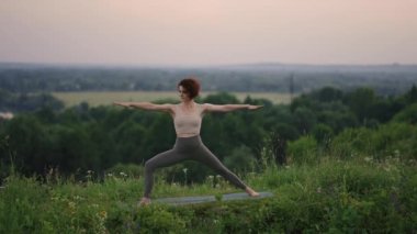 Genç bir kadın, ormanın tepesinde bir nehrin arka planına ve orman manzarasına karşı yoga egzersizleri yapıyor. Beden ve ruh dengesi, rahatlama ve meditasyon 