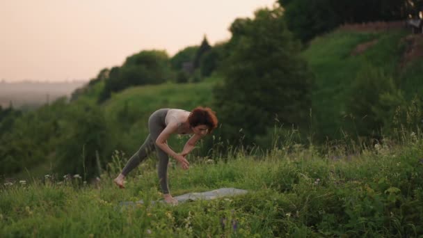 Un maestro de yoga hace ejercicios de equilibrio y estiramiento. La paz y suavidad de los movimientos de una chica haciendo yoga en las montañas en el bosque — Vídeo de stock