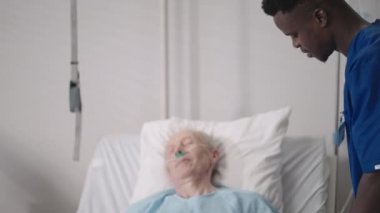 Afrikalı etnik grup doktorlarından oluşan bir ekip yaşlı bir erkek ve kadınla konuşuyor. Bir doktor ve bir hemşire hastane koğuşunda yatalak bir hastayla konuşuyorlar.