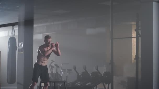 Slow motion: Muscular Shirtless Fit Man Energetically Box Jumps in Hardcore Gym doing Part of His Cross Fitness Training Plan. Man is Sweaty from Intense Workout — Stock Video