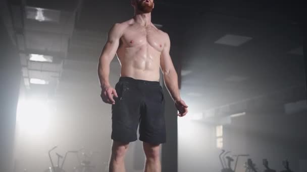 スローモーション:筋肉のないシャープなフィット男ハードコアジムで精力的にボックスジャンプ彼のクロスフィットネストレーニングプランの一部をやっています。男は激しいトレーニングから汗をかく — ストック動画