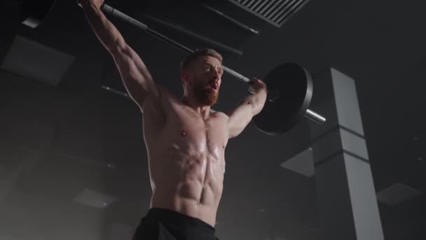 Slow motion: Brutal athlete lifts the bar above himself, performing a jerk, a spinning push. A man is engaged in weightlifting on a dark background, portrait. Concept strength, power, playing sports. — Stock Video