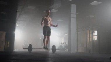 Tanınmış kasları olan genç bir atletik spor salonunda ağır çekimde ipe atlıyor.