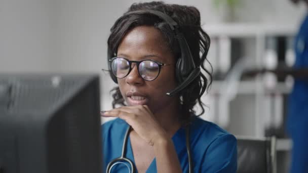 Afroamerykanka czarny kobieta lekarz ogólny w białym płaszczu siedzi za biurkiem w gabinecie lekarzy i przewijanie myszy komputerowej podczas czytania pacjentów historii medycznej — Wideo stockowe