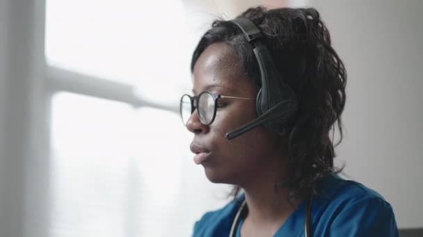 Afro-Américaine noire omnipraticienne en manteau blanc assise au bureau des médecins et faisant défiler la souris d'ordinateur tout en lisant les antécédents médicaux des patients — Video