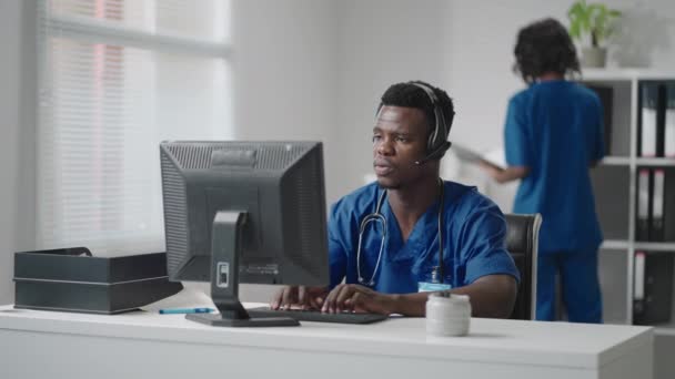 Ärzte Online-Arztkonsultation: Afroamerikanischer Arzt führt eine Videokonferenz mit einem Patienten auf einem Desktop-Computer durch. — Stockvideo