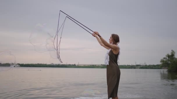 Uma jovem artista mostra truques mágicos usando enormes bolhas de sabão. Criar bolhas de sabão usando paus e corda ao pôr do sol para mostrar um show de circo teatral — Vídeo de Stock