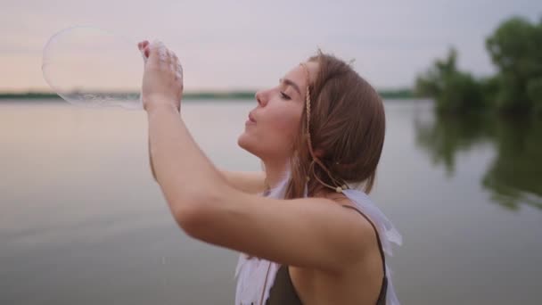 Een jonge meisje kunstenaar toont magische trucs met behulp van zeepbellen. Maak zeepbellen in je handen en blaas ze locatie theatrale circus show bij zonsondergang — Stockvideo