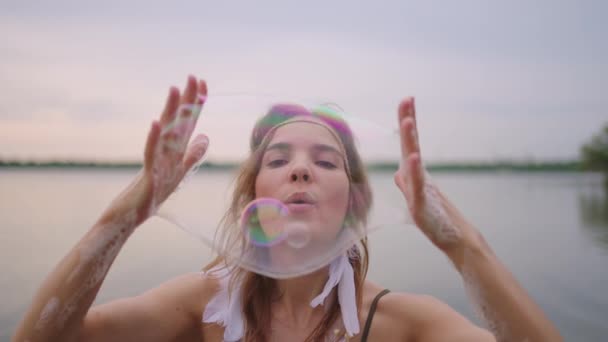 Eine junge Künstlerin zeigt Zaubertricks mit Seifenblasen. Erstellen Sie Seifenblasen in Ihren Händen und blasen Sie sie auf Ort theatralische Zirkusshow bei Sonnenuntergang — Stockvideo