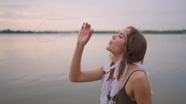 En ung kvinnlig konstnär visar en såpbubbla show genom att blåsa upp stora såpbubblor med händerna i slow motion — Stockvideo