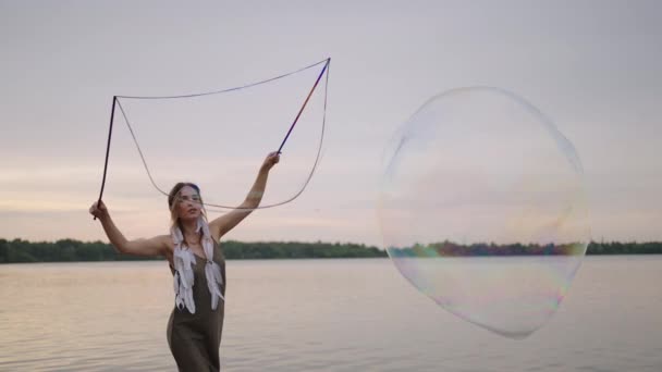 Eine junge Künstlerin zeigt Zaubertricks mit riesigen Seifenblasen. Erstellen Sie Seifenblasen mit Stöcken und Seil bei Sonnenuntergang, um eine theatralische Zirkusshow zu zeigen — Stockvideo