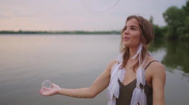 Genç bir kadın sanatçı, sabun köpüklerini yavaş çekimde şişirerek bir dizi gösteriyor.