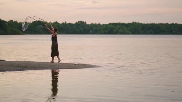 Egy fiatal női művész egy szappanbuborék show-t mutat, ami hatalmas szappanbuborékokat robbant fel egy tó partján naplementekor. Mutasd meg a gyönyörű show szappanbuborékok lassított felvételen — Stock videók