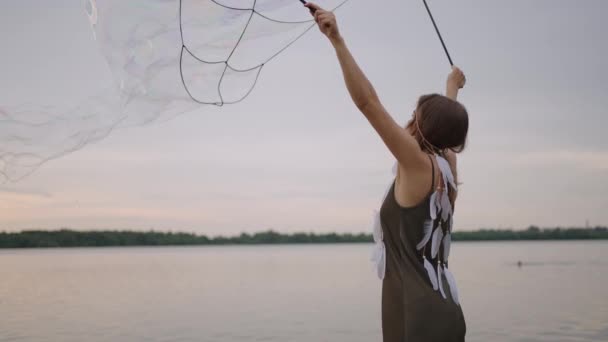 Una joven artista muestra trucos de magia usando enormes burbujas de jabón. Crear burbujas de jabón utilizando palos y cuerda al atardecer para mostrar un espectáculo de circo teatral — Vídeos de Stock