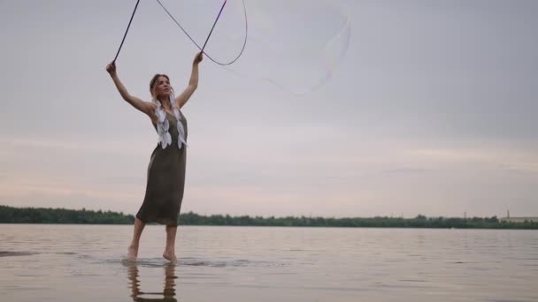 Een jonge meisje kunstenaar toont magische trucs met behulp van enorme zeepbellen. Maak zeepbellen met stokken en touw bij zonsondergang om een theatrale circusshow te tonen — Stockvideo