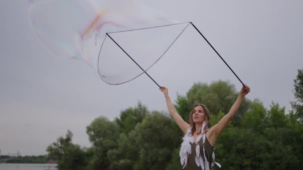 Молода дівчина художник показує магічні трюки, використовуючи величезні мильні бульбашки. Створити мильні бульбашки за допомогою паличок і мотузки на заході сонця, щоб показати театральне циркове шоу — стокове відео