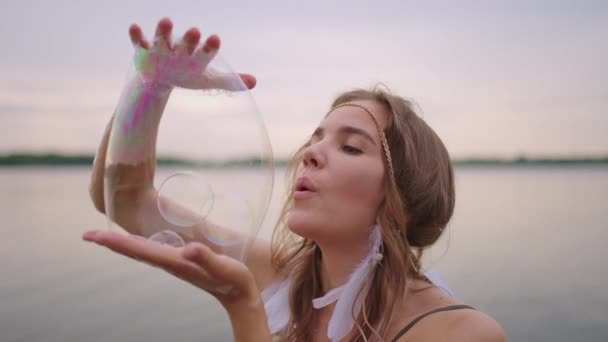 若い女性アーティストは、スローモーションで彼女の手で大きなシャボン玉を爆破することによって石鹸バブルショーを示しています — ストック動画